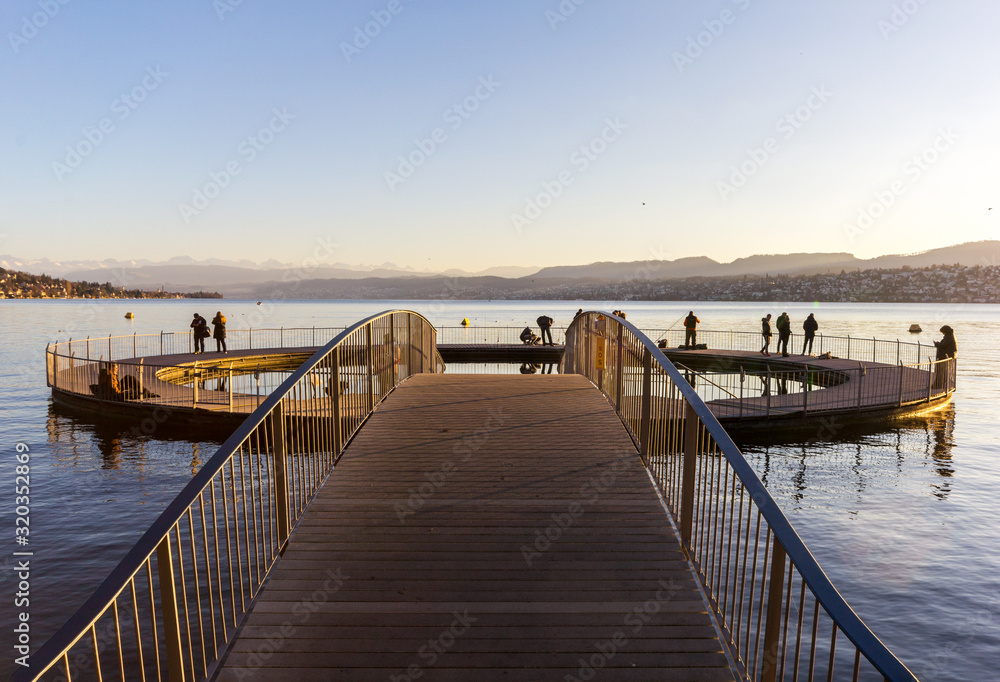 Fototapeta premium Zurich, Switzerland - January 02, 2020: The circle form public swimming pool at the Lake Zurich in winter season with people walking on it