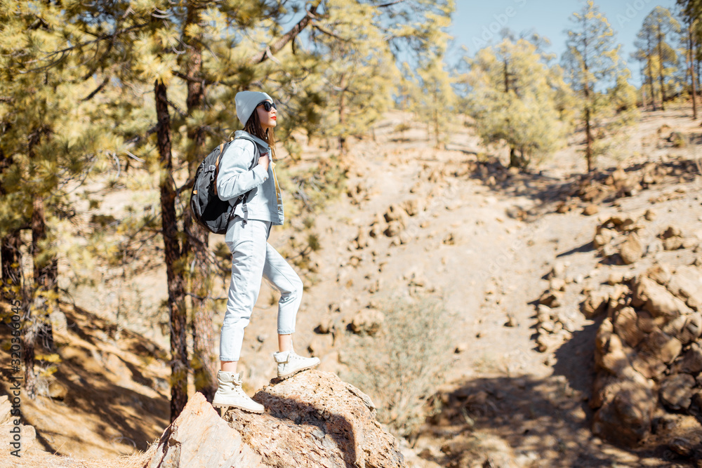 Stylish woman enjoying beautiful landscapes on volcanic rocks in the pine woods, traveling high in the mountains on Tenerife island, Spain Stylish woman enjoying beautiful landscapes on volcanic rocks in the pine woods, traveling high in the mountains on Tenerife island, Spain