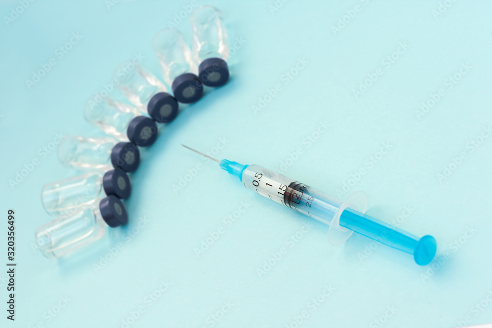 Glass medicine bottles with injection fluid with blue aluminium caps and syringe for vaccination. Cancer, painand diabetes treatment, pharmaceutical medicine concept . Glass medicine bottles with injection fluid with blue aluminium caps and syringe for vaccination. Cancer, painand diabetes treatment, pharmaceutical medicine concept .