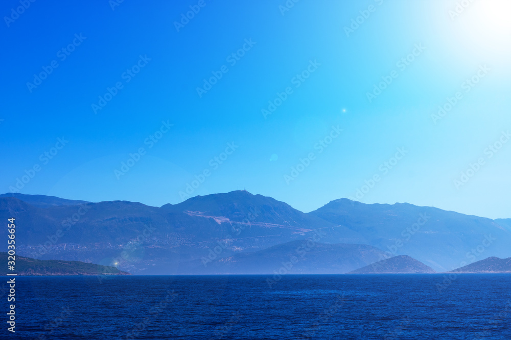 Creative layout made of seascape with mountains in fog and bright sunbeams, touristic season. Mediterranian calm sea.