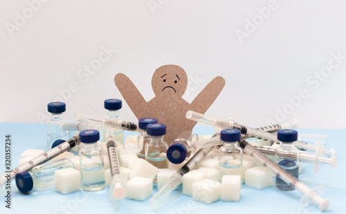 Sugar addiction, insulin resistance,   cardboard man surrounded by refined sugar cubes, syringe for vaccination and bottles of insulin on white background, diabetes protection medical concept.