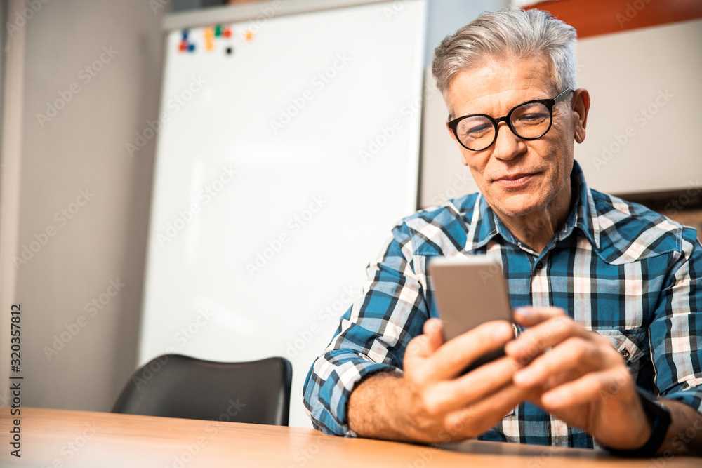 Smiling adult male looking at smartphone screen in the office Smiling adult male looking at smartphone screen in the office
