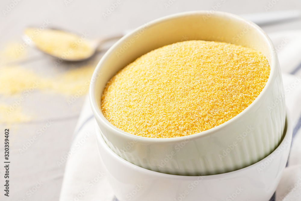 Dry uncooked polenta in bowls on the table, light background, space for text. Dry uncooked polenta in bowls on the table, light background, space for text.