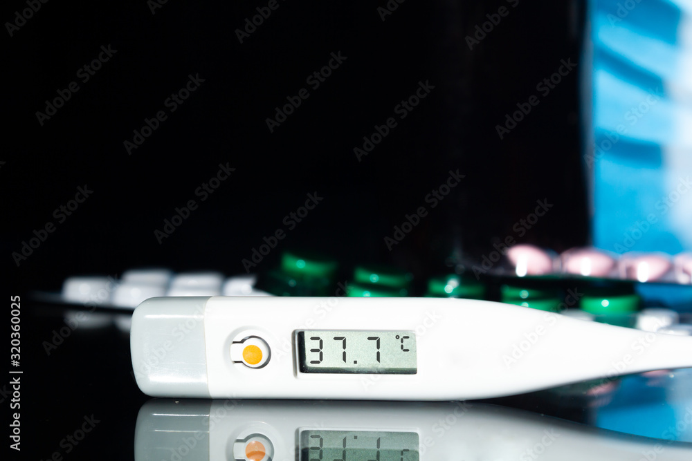 medical jars, thermometer, syringe, gauze mask and pills medicines, medicine on a thermometer 37.7 degrees Celsius on glass black background close up. copy space