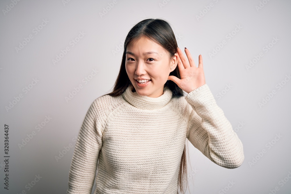 Young beautiful asian woman wearing casual sweater standing over isolated background smiling with hand over ear listening an hearing to rumor or gossip. Deafness concept. Young beautiful asian woman wearing casual sweater standing over isolated background smiling with hand over ear listening an hearing to rumor or gossip. Deafness concept.