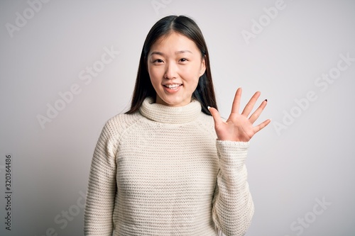 Young beautiful asian woman wearing casual sweater standing over isolated background showing and pointing up with fingers number five while smiling confident and happy.