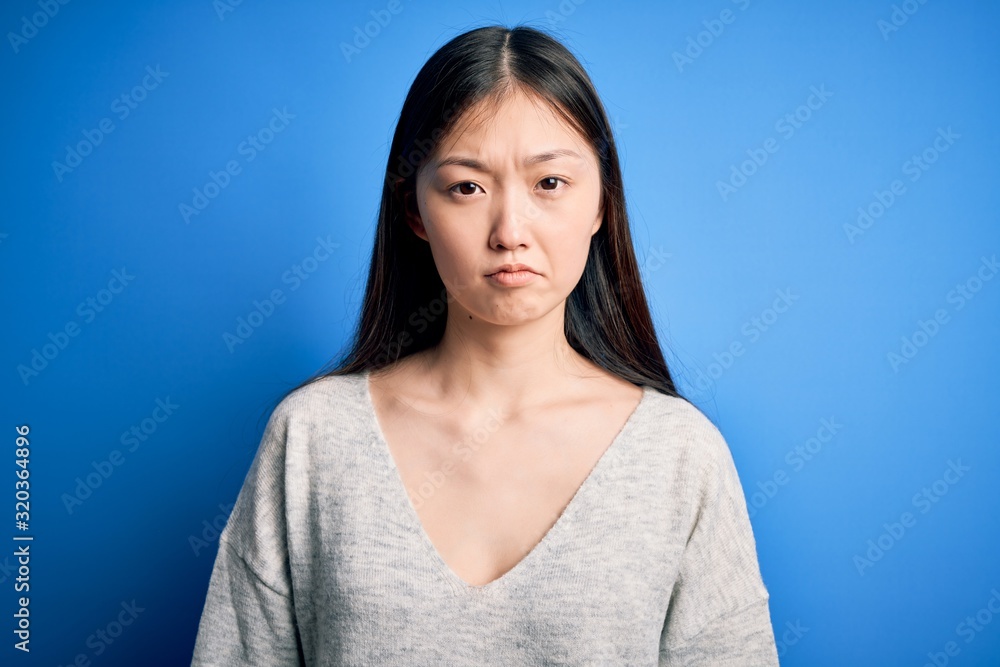 Young beautiful asian woman wearing casual sweater standing over blue isolated background depressed and worry for distress, crying angry and afraid. Sad expression. Young beautiful asian woman wearing casual sweater standing over blue isolated background depressed and worry for distress, crying angry and afraid. Sad expression.