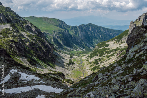 Panoramic view of a beautiful green valley with a flowing river through it and steep rocky slopes descending to it  in the background in the distance is Vitosha Mountain  Rila Mountain  Bulgaria