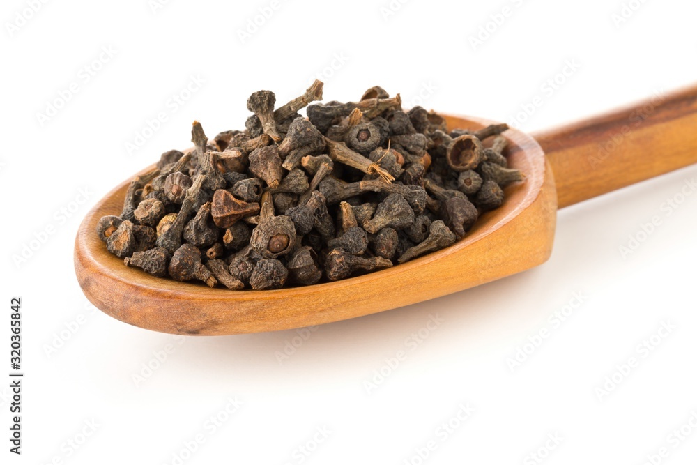 Heap of raw, dried cinnamon blossom buds spice in wooden spoon over white Heap of raw, dried cinnamon blossom buds spice in wooden spoon over white