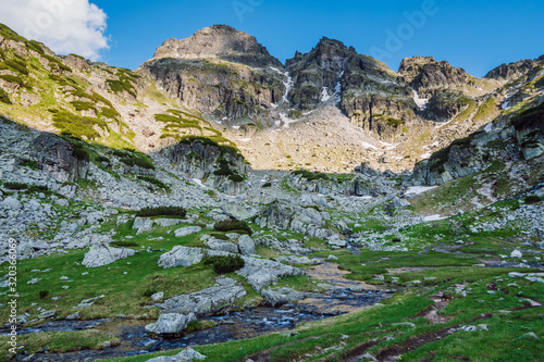 View of a beautiful green mountain valley with small river running through it and high rocky peaks hanging over it, Malyovitsa hiking trail, Rila mountain, Bulgaria.