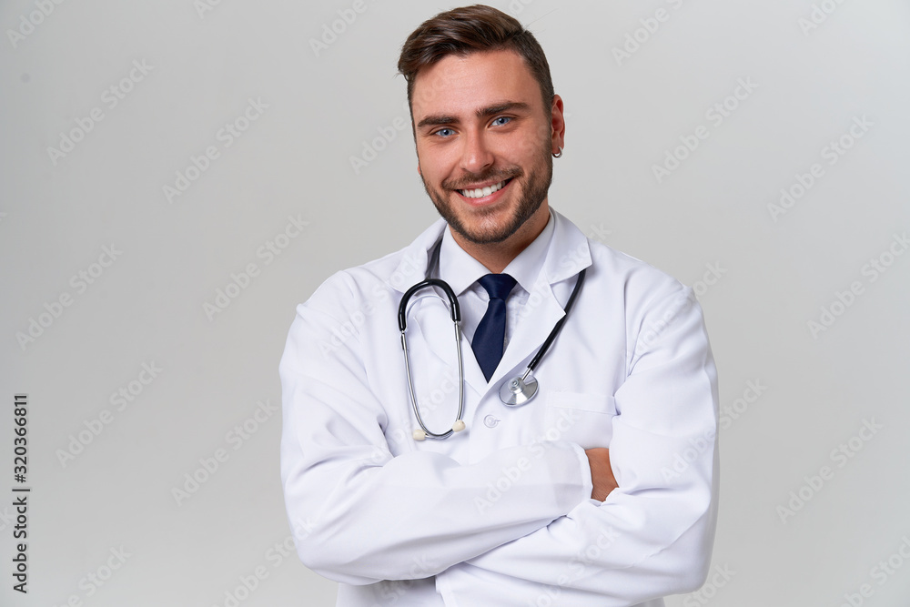Young handsome modern doctor in a white medical gown stands in the studio on a white background. Student trainee of a medical university. Young handsome modern doctor in a white medical gown stands in the studio on a white background. Student trainee of a medical university.