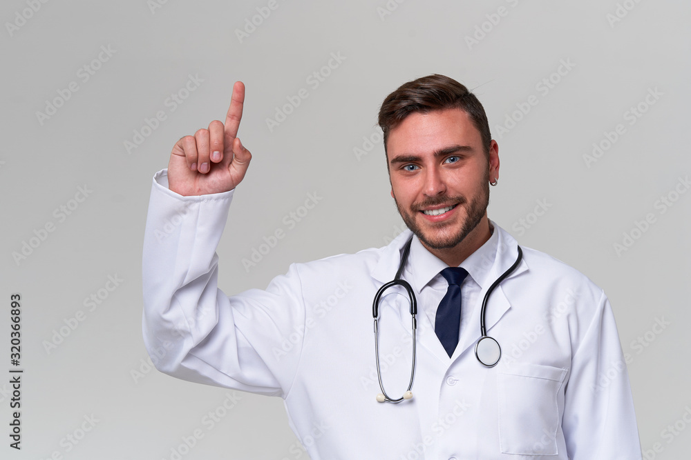 Young handsome modern doctor in a white medical gown stands in the studio on a white background. Student trainee of a medical university. Young handsome modern doctor in a white medical gown stands in the studio on a white background. Student trainee of a medical university.