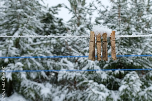 Snowfall in russian countryside. Wooden vintage clothespins covered with slightly mould  due weather wetness on a clothesline with a blurred background of everygreen trees. Wooden clothes pegs. photo