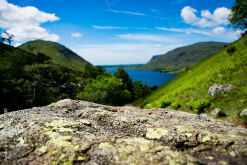 A close up of a moss covered textured rock with an out of focus mountainous and lake background.