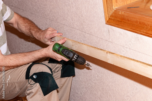 Man works with cordless screwdriver on a wall in the house