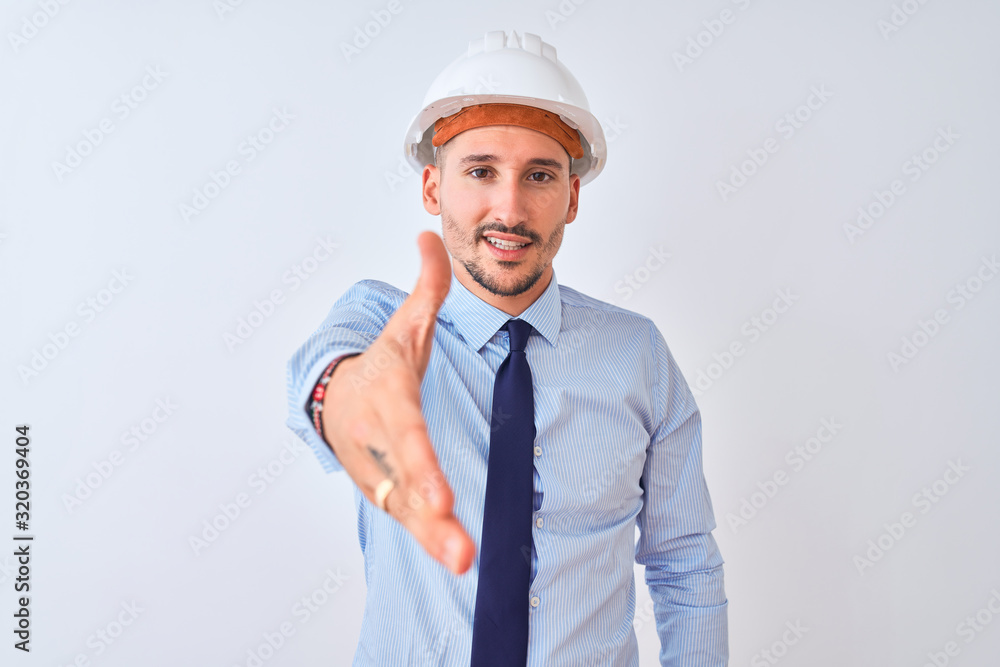 Young business man wearing contractor safety helmet over isolated background smiling friendly offering handshake as greeting and welcoming. Successful business. Young business man wearing contractor safety helmet over isolated background smiling friendly offering handshake as greeting and welcoming. Successful business.