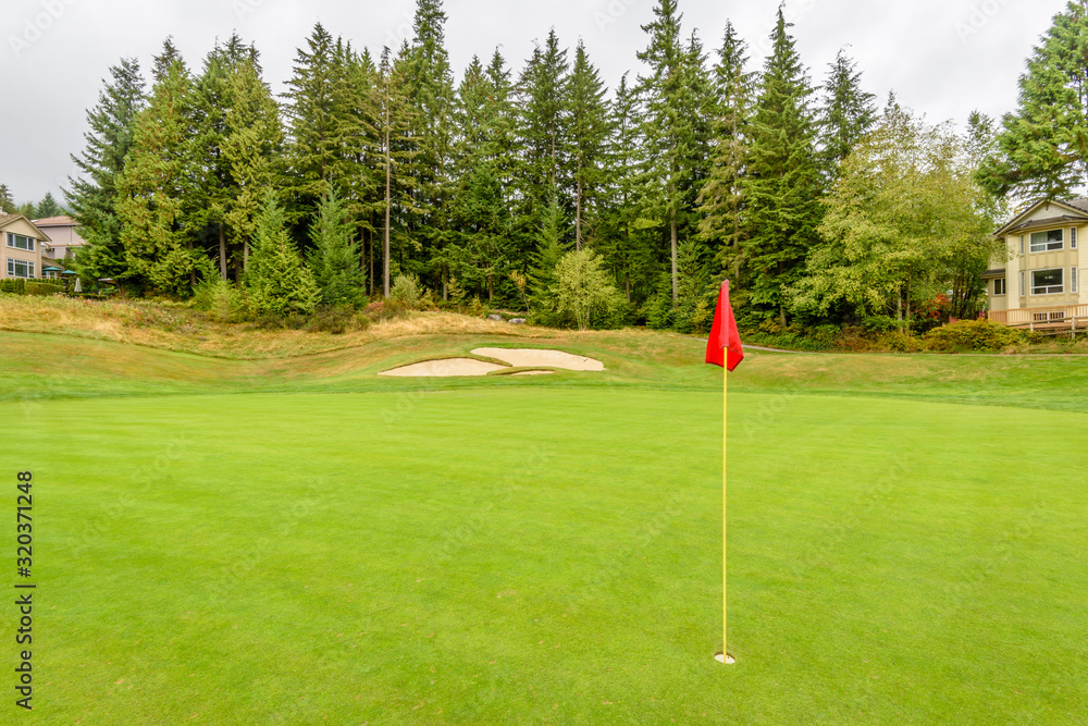 Obraz premium Golf course with gorgeous green, sand bunker and golf flag and real estate on background.