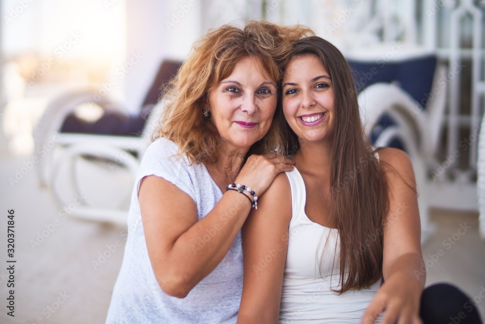 Fototapeta premium Beautiful mother and daugther sitting at terrace hugging and smiling