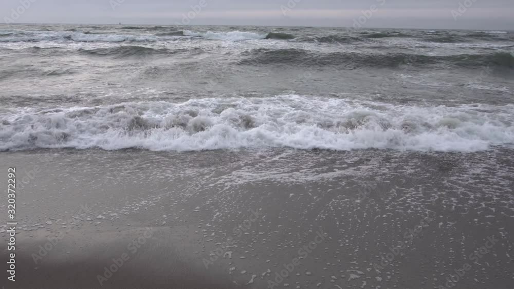 White waves splashing on the dark sand beach coast in the evening Baltic sea, low angle White waves splashing on the dark sand beach coast in the evening Baltic sea, low angle