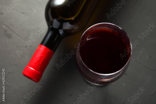 a glass of grape wine next to a sealed bottle of wine on a dark table