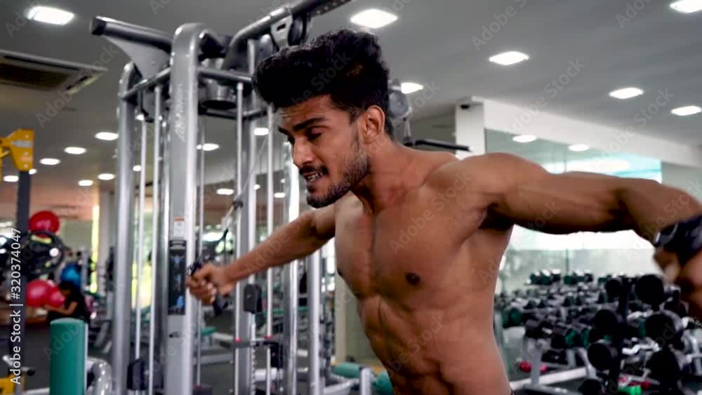 Young asian man using a cross cable training machine in gym Young asian man using a cross cable training machine in gym