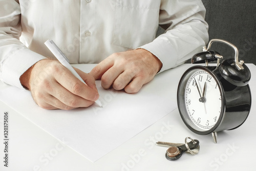 Man signs a blank sheet of document. The contract of sale or deed of gift for the apartment. Alarm clock close-up with the passing time.