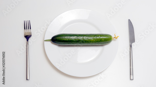 The concept of diet and healthy lifestyle. Top view of a plate in which lies a cucumber, with a fork and a knife, is on the table. © Michael