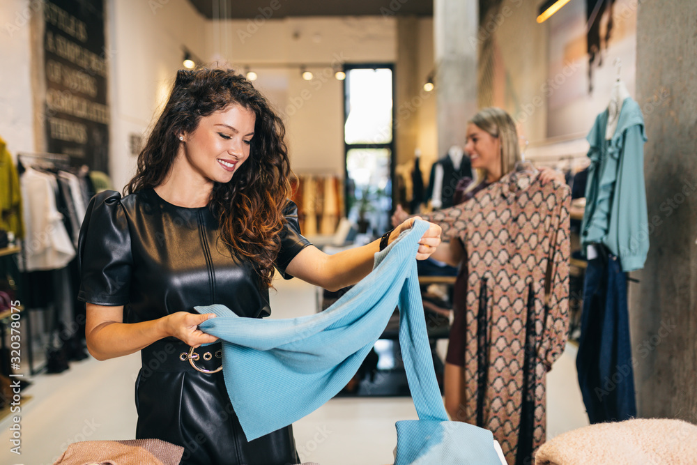 Beautiful young women trying elegant clothes in expensive boutique