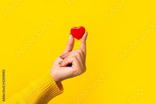 Hand holding a red heart over yellow background, heart health, and donation concepts