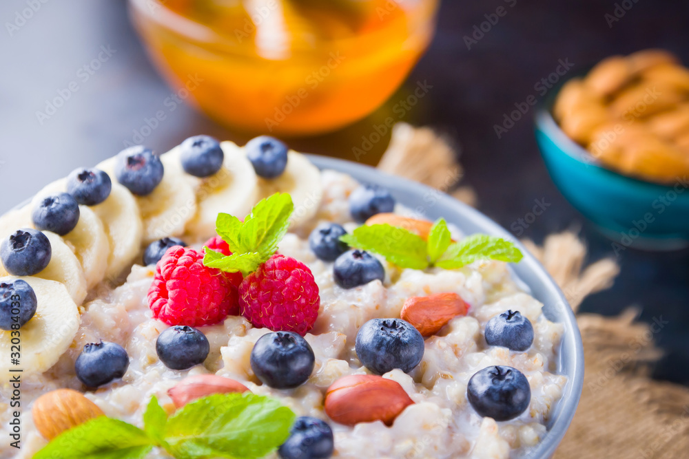 Oatmeal porridge with berries, fruits and honey on dark background. Oatmeal with raspberries, blueberries and almonds on burlap. Healthy breakfast Oatmeal porridge with berries, fruits and honey on dark background. Oatmeal with raspberries, blueberries and almonds on burlap. Healthy breakfast