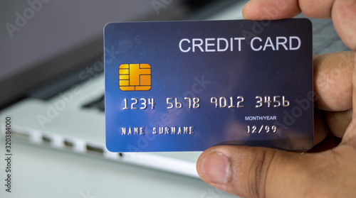 Close up holding a blue credit card placed in front of the laptop. online shopping payment and retail concepts. mockup and fake credit card