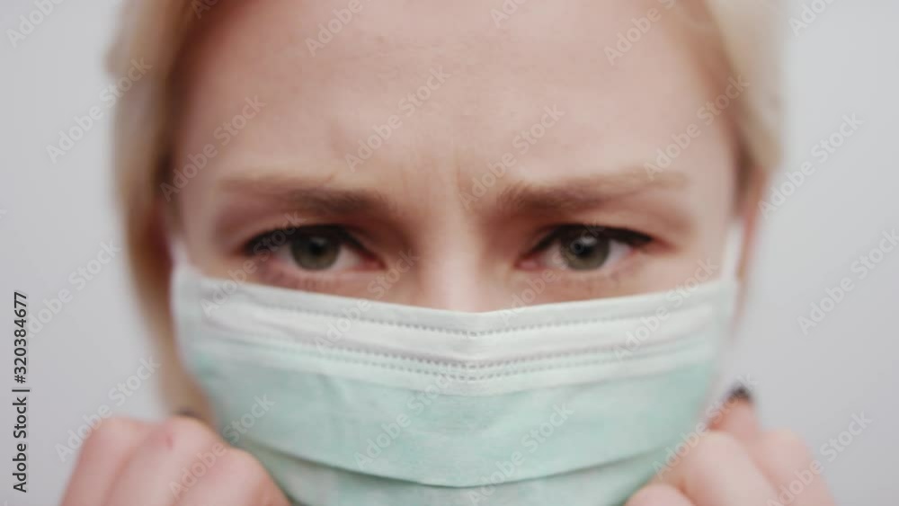 Woman in mask protecting against influenza flu virus putting her hands to face, looking straight into her eyes, medical hospital mask on