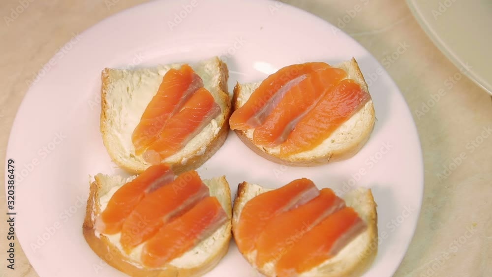 Female hand puts slices of red fish on sandwiches with butter Female hand puts slices of red fish on sandwiches with butter