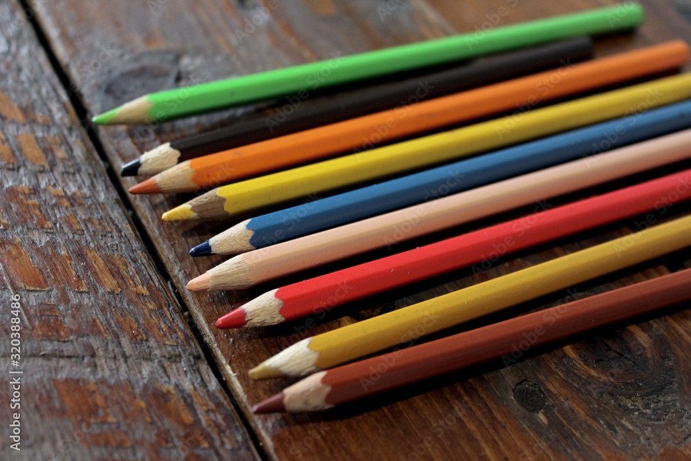 Colored pencils lying on the wooden table, ready to draw and make art as part of creative hobby and leisure time Colored pencils lying on the wooden table, ready to draw and make art as part of creative hobby and leisure time