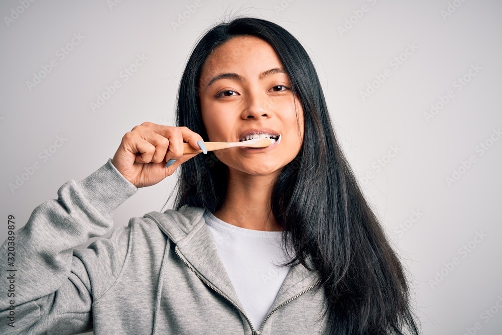 Young beautiful woman smiling happy. Standing with smile on face whasing tooth using toothbrush over isolated white background Young beautiful woman smiling happy. Standing with smile on face whasing tooth using toothbrush over isolated white background