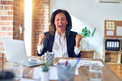 Middle age beautiful businesswoman working using laptop at the office celebrating surprised and amazed for success with arms raised and open eyes. Winner concept.
