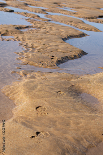 footprints of bare feet running along the beach between puddles