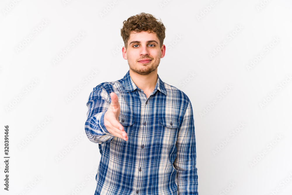 Young blond curly hair caucasian man isolated stretching hand at camera in greeting gesture. Young blond curly hair caucasian man isolated stretching hand at camera in greeting gesture.