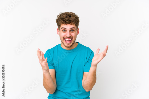 Young blond curly hair caucasian man isolated celebrating a victory or success, he is surprised and shocked.