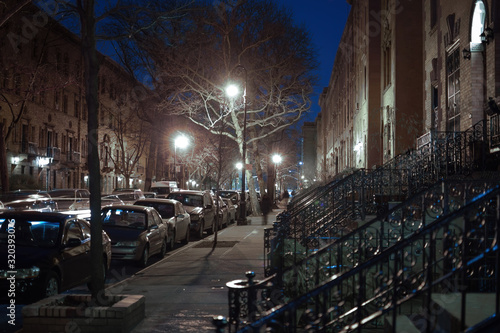 Nighttime shot, looking down a small street, with street lamps, trees, and building facade in Harlem, New York, NY, USA