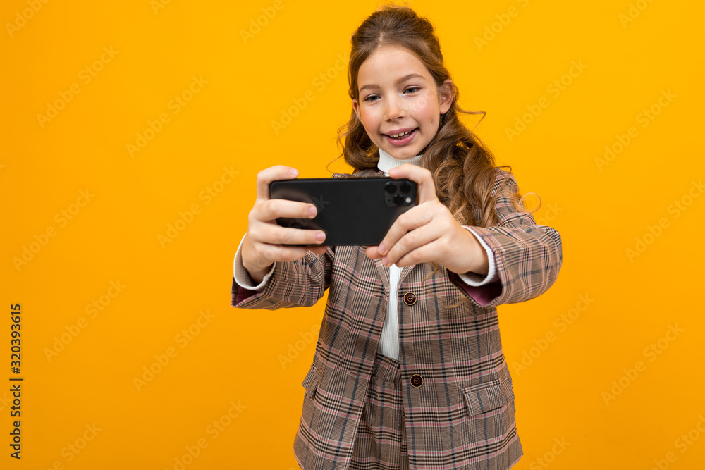 laughing stylish blonde caucasian girl in a classic jacket takes a photo on a smartphone on a yellow studio background laughing stylish blonde caucasian girl in a classic jacket takes a photo on a smartphone on a yellow studio background