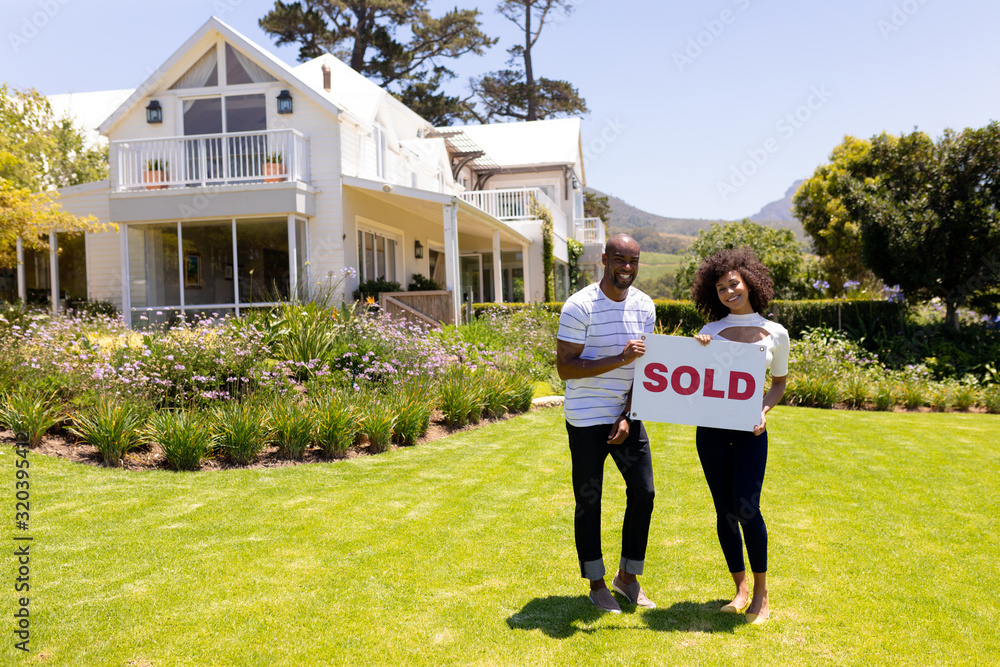 Happy young couple in the garden holding sold sign