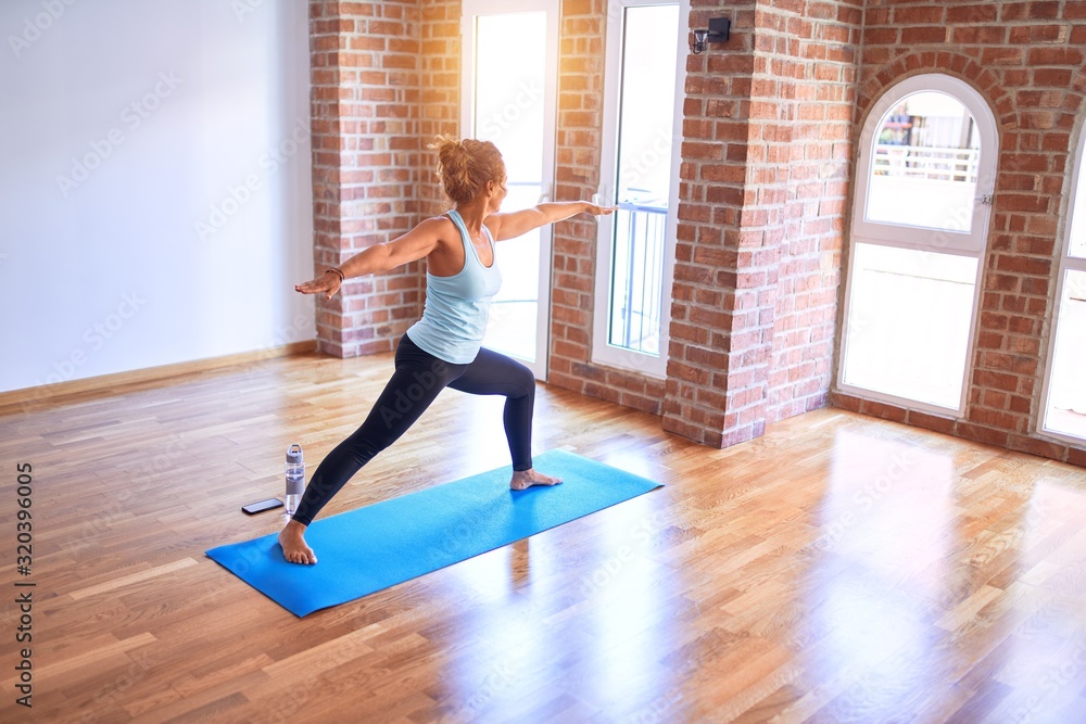 Middle age beautiful sportwoman standing on mat. Practicing yoga doing warrior pose at gym Middle age beautiful sportwoman standing on mat. Practicing yoga doing warrior pose at gym