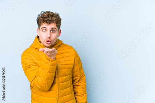 Young blond curly hair caucasian man isolated folding lips and holding palms to send air kiss.