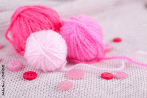 Pink balls of yarn of different sizes and buttons on a gray knitted background. Handicraft, needlework, hobby, knitting, DIY