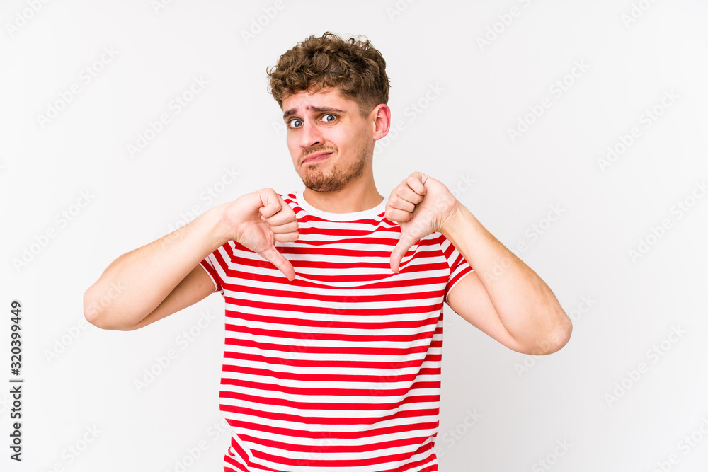 Young blond curly hair caucasian man isolated showing thumb down, disappointment concept. Young blond curly hair caucasian man isolated showing thumb down, disappointment concept.