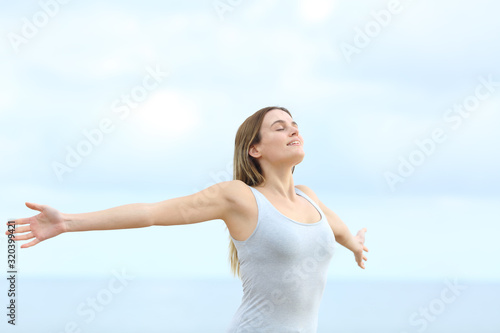 Happy woman breathing fresh air outstretching arms on the beach