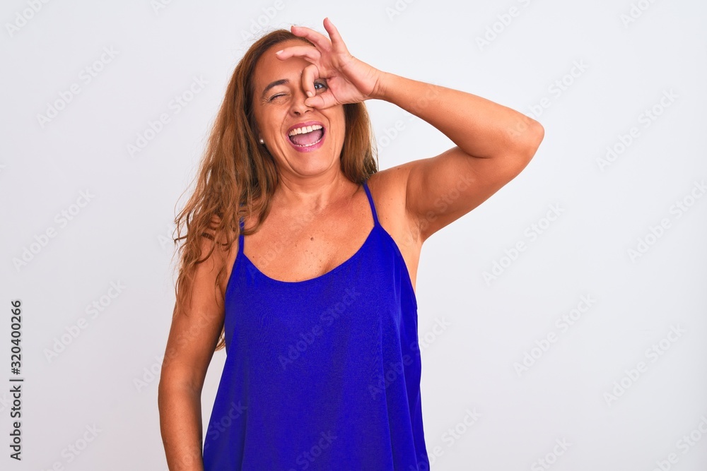 Middle age mature woman standing over white isolated background doing ok gesture with hand smiling, eye looking through fingers with happy face. Middle age mature woman standing over white isolated background doing ok gesture with hand smiling, eye looking through fingers with happy face.