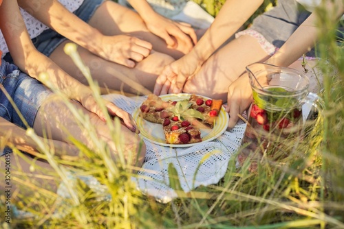 Children sitting on grass eating homemade cake with berries, drinking mint strawberry drink