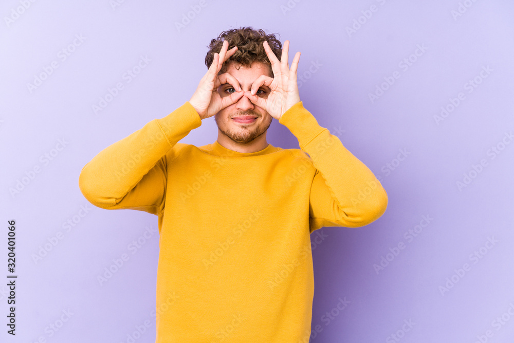 Young blond curly hair caucasian man isolated showing okay sign over eyes Young blond curly hair caucasian man isolated showing okay sign over eyes